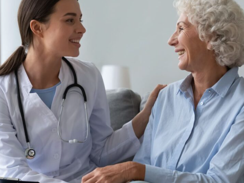 A doctor in a white coat gently places a hand on an older woman’s shoulder during a calm healthcare visit, offering support while discussing dental issues related to metallic taste in mouth dental causes.