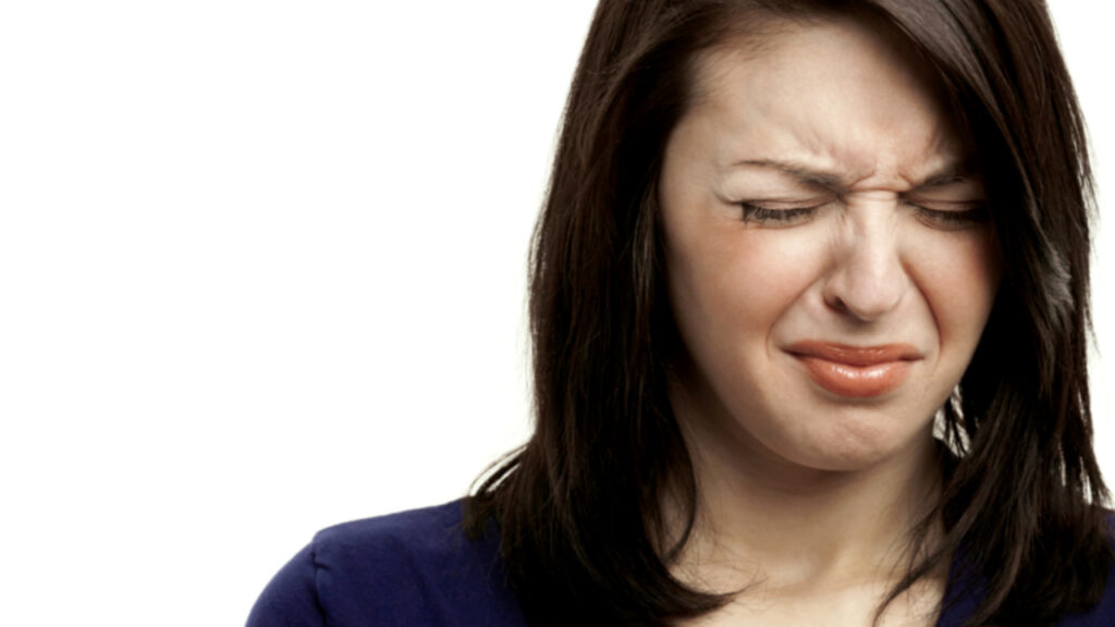 Woman reacting strongly to an unpleasant or distorted taste, representing symptoms of dysgeusia.