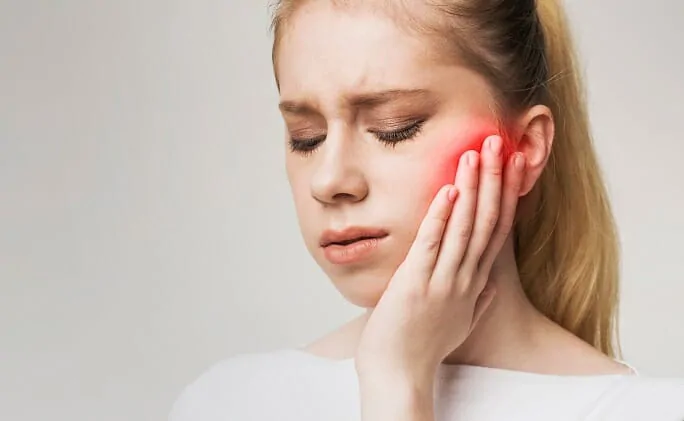 Woman holding her cheek in discomfort, showing symptoms of jaw-pain-after-sleeping.