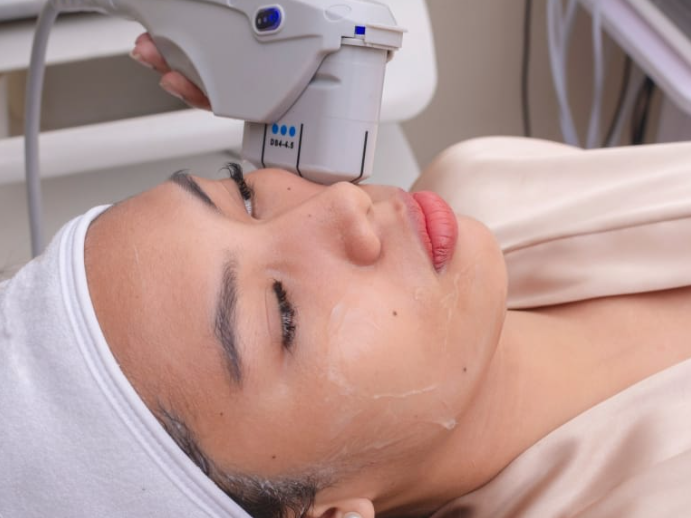 HIFU ultrasound device being used on a woman’s face during a non-surgical skin tightening treatment in a clinic.