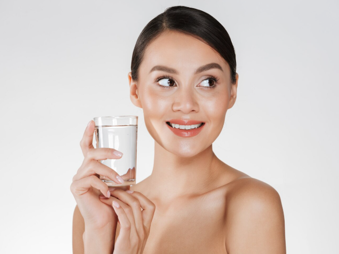 Awoman with healthy skin holding a glass of water, representing hydration for skin health.